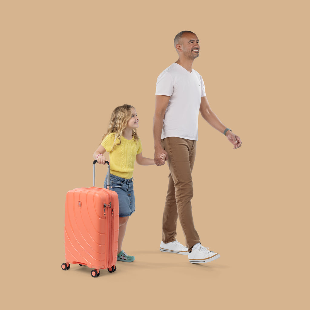 Father walking with daughter while daughter holds handle of coral orange carry on luggage