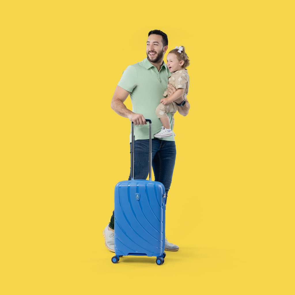 father carrying daughter while holding handle of ocean blue carry on luggage