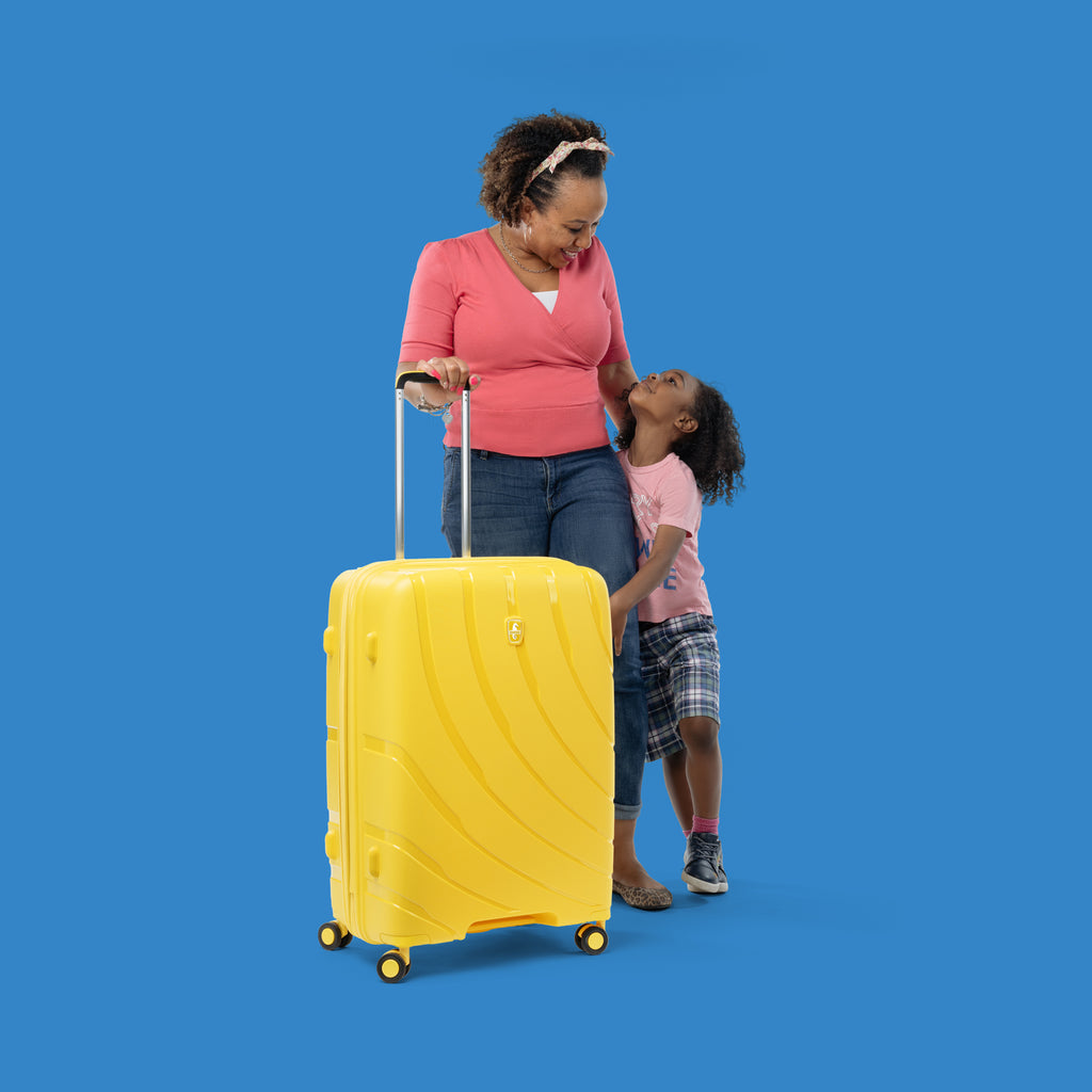 mother standing next to son while holding handle of sunshine yellow medium to large checked in luggage