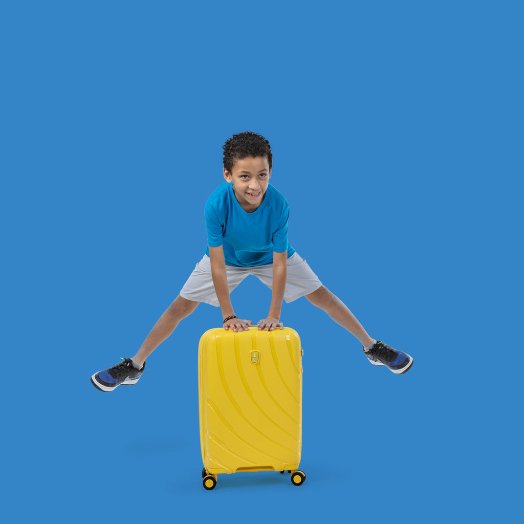 boy hopping over sunshine yellow carry-on suitcase
